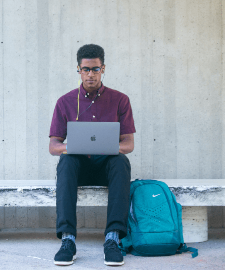 male student sitting outside building with laptop